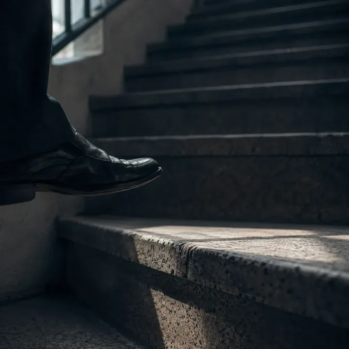 Pé de sapato social pairando acima do primeiro degrau de uma escada de prédio antigo